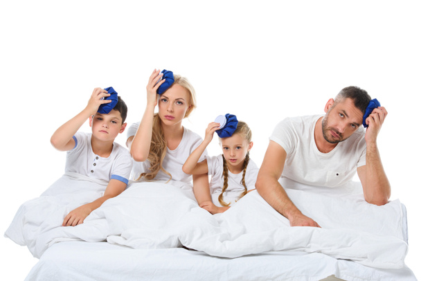 ill family holding ice packs on heads while sitting in bed, isolated on white - Photo, Image