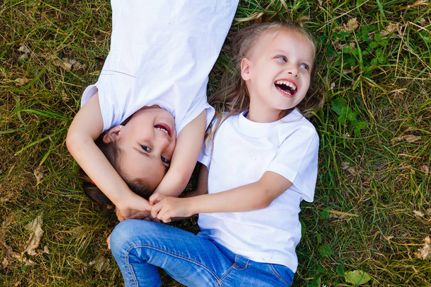Two little girls in white T-shirts lay on the grass in the park. view from above - Photo, Image