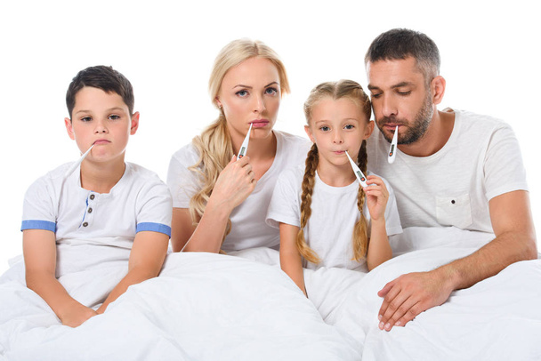 αναστατωμένος άρρωστος οικογένεια με ηλεκτρονικά θερμόμετρα κάθεται στο κρεβάτι, απομονώνονται σε λευκό - Φωτογραφία, εικόνα