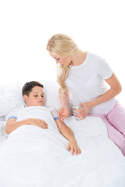 mother giving pills and glass of water to ill son, isolated on white - Photo, Image
