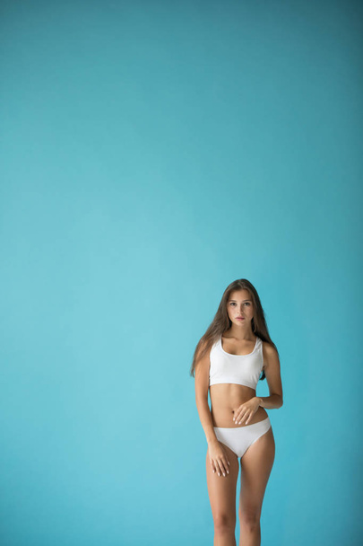 Attractive young woman in white sport underwear on a blue background. - Foto, Imagen