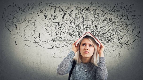 Confused young woman student holding a opened book over head. Stressed emotion, unhappy feeling, difficult task to solve. Hundreds of arrows and curves mess, anxiety and headache. - Photo, Image