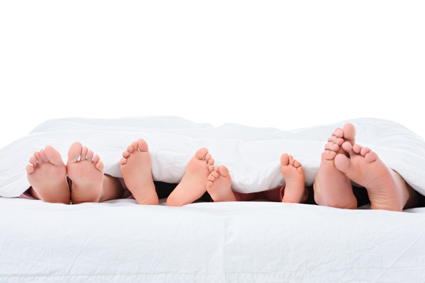 Eltern und Kinder Füße im Bett unter einer weißen Decke, isoliert auf weiß - Foto, Bild