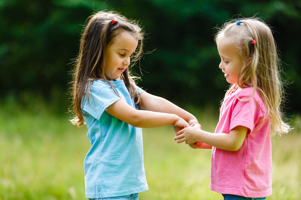 Two little girls stand opposite each other holding hands in the Park - Φωτογραφία, εικόνα