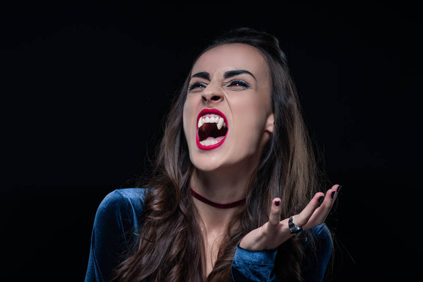 grim woman showing vampire fangs isolated on black - Photo, Image