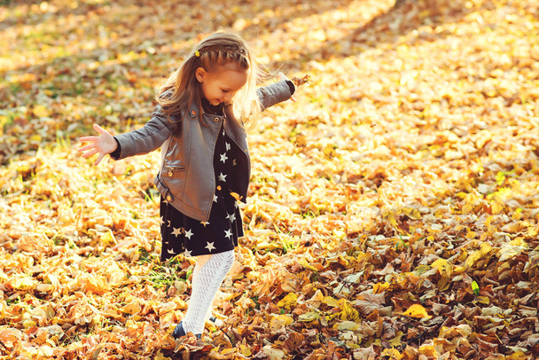 Happy child walking in autumn park. Baby girl throwing the fallen leaves up. Beautiful golden autumn time. Happy and healthy childhood. Autumn kids fashion. Autumn holidays - Photo, Image