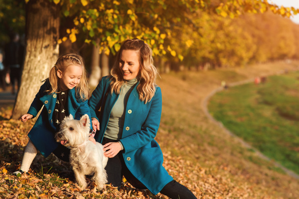 Anya és kis lánya őszi séta kutyával. Kint boldog családi portré. Őszi divat. A kislányom elegáns és gyönyörű édesanyja. Boldog gyermekkor - Fotó, kép