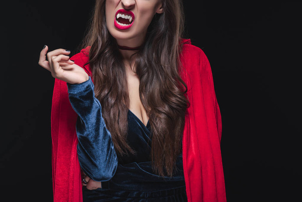 cropped view of vampire woman in red cloak showing her fangs isolated on black - Zdjęcie, obraz
