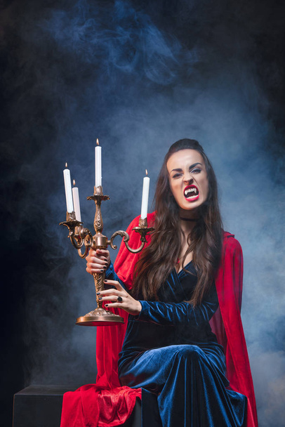 vampier vrouw met antieke kandelaar op duisternis met rook  - Foto, afbeelding