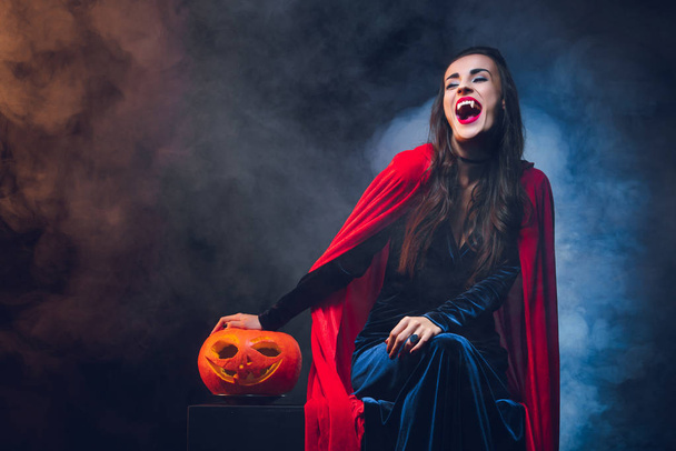 schöne Frau im Vampirkostüm lächelt auf dunklem Hintergrund mit Rauch  - Foto, Bild