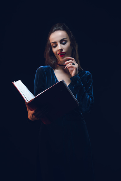 Sexy vampire woman holding magic book isolated on black - Photo, Image