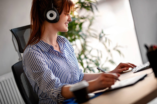 Smiling female designer listening music while working on computer in office - 写真・画像