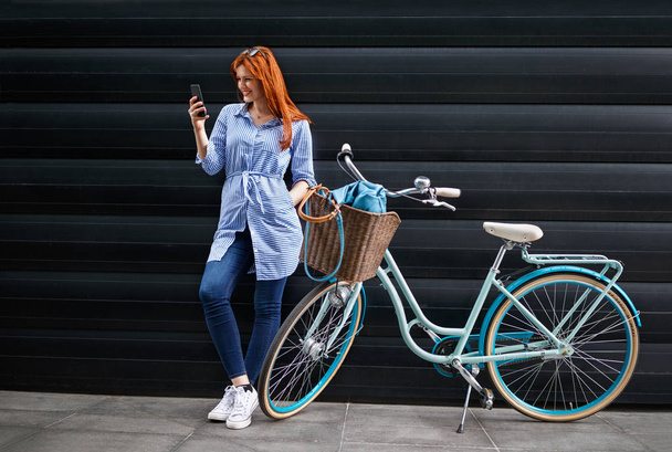 Молодая женщина смотрит на сотовый телефон рядом с велосипедом
 - Фото, изображение