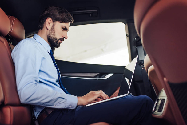 side view of caucasian businessman using laptop computer in the car - Foto, afbeelding