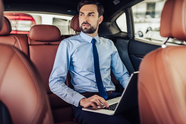 portrait of young bearded businessman working on laptop computer in the car and looking away - Photo, Image