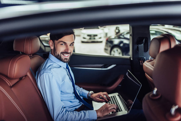 caucasian businessman working on laptop computer in the car and lookin at the camera - Фото, изображение