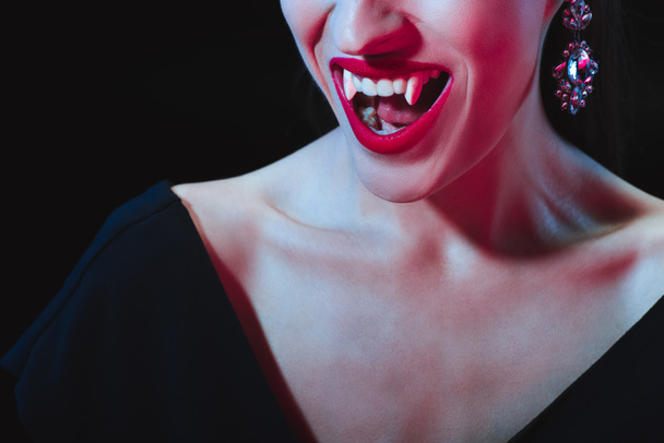 bijgesneden weergave van vampier tonen haar tanden geïsoleerd op zwart - Foto, afbeelding