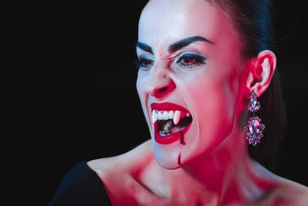 Vampir zeigt ihre Reißzähne und schaut isoliert auf schwarz weg - Foto, Bild
