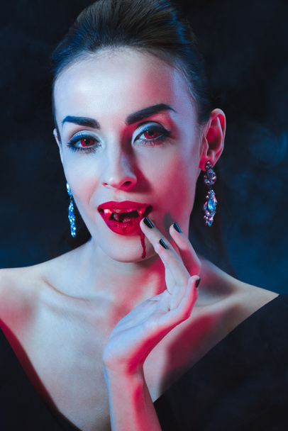 sexy vampire woman licking her fingers on dark background with smoke  - Фото, зображення