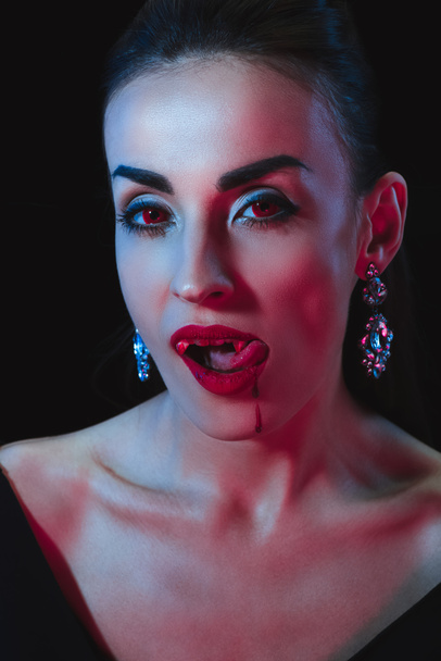 beautiful vampire woman licking her lips on dark background - Foto, Imagem