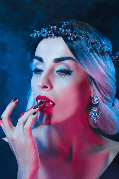 sexy vampire woman licking blood from fingers on dark background with smoke  - Valokuva, kuva