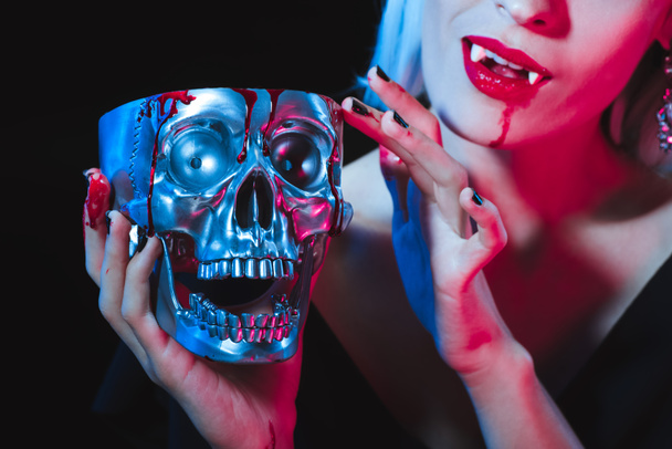 обрезанный вид вампира, держащего металлический череп с кровью, изолированной на черном
 - Фото, изображение