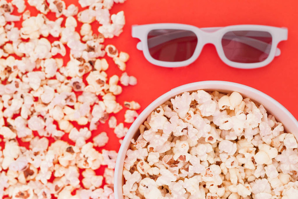 White 3d glasses paper cup and fresh cheesy popcorn on a red background, top view, copyspace. Cinema Concept. - Foto, Imagem