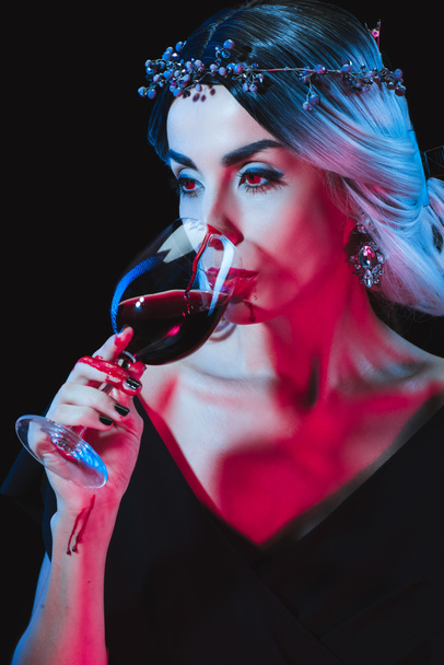 όμορφο βαμπίρ που πίνει αίμα από wineglass απομονώνονται σε μαύρο - Φωτογραφία, εικόνα
