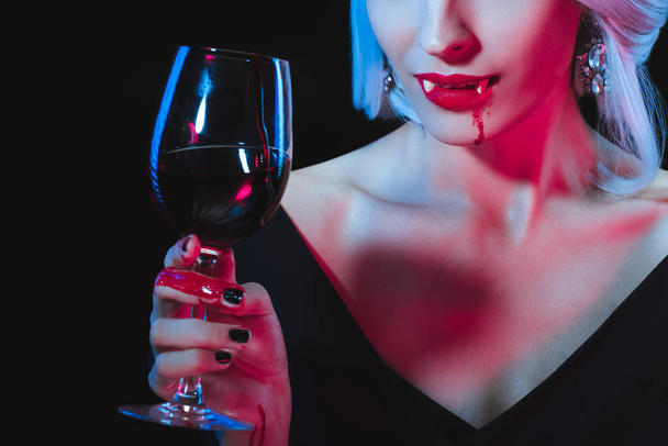обрезанный вид женщины-вампира, держащей бокал с кровью, изолированной на черном
 - Фото, изображение