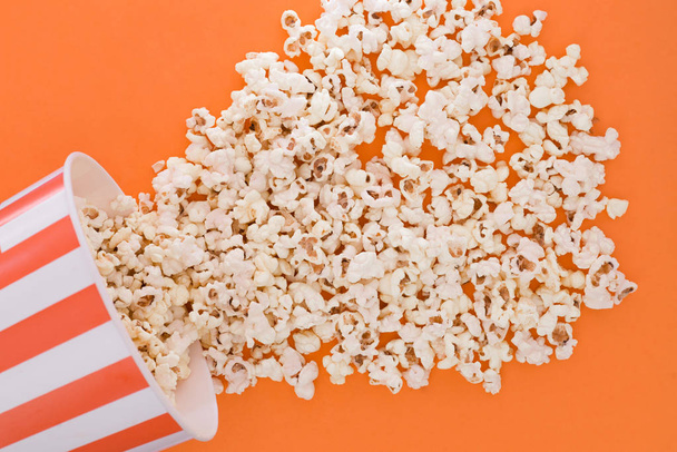 Popcorn rises from a paper bowl to a orange background, a view from above. Cup with popcorn is isolated on a orange background. Flat lay. Copyspace. Cinema Concept. - Foto, imagen