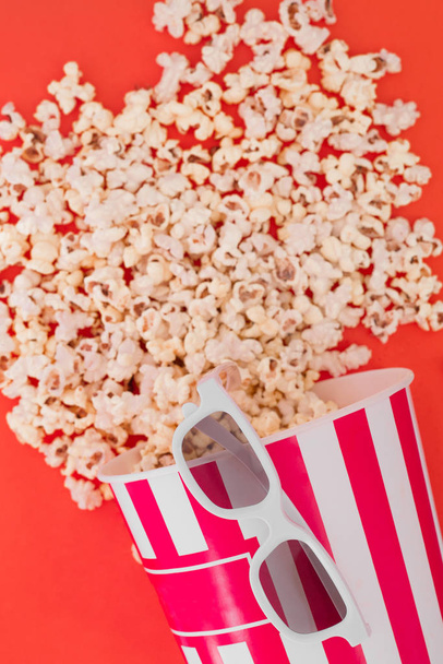 Popcorn egy papír tálba, és a 3D-s szemüveg a filmet egy piros hátteret, felülnézet. Lapos feküdt. Copyspace. Mozi-koncepció. - Fotó, kép