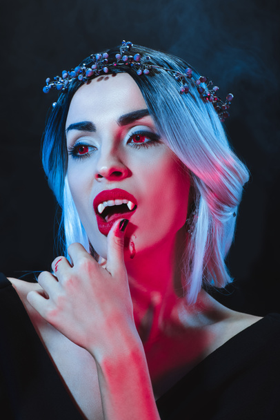 красива вампірська жінка торкається її губ на темному тлі з димом
  - Фото, зображення