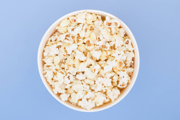 Popcorn in a paper cup is isolated on a pastel blue background, a view from above. Flat lay. Copyspace. Background. Cinema Concept - Фото, изображение