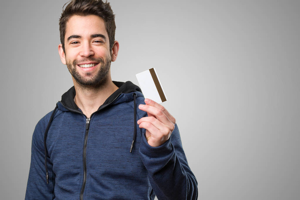 young man holding a credit card on grey background - Photo, Image