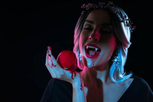 містична вампірська жінка кусає червоне криваве яблуко ізольовано на чорному
 - Фото, зображення