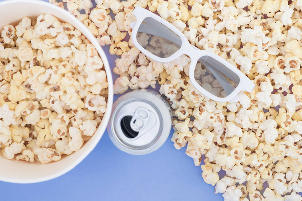 Білі 3d окуляри, металева банка з напоєм, паперова чашка та свіжий сирний попкорн на пастельному синьому фоні, вид зверху, копія. Концепція кіно
. - Фото, зображення