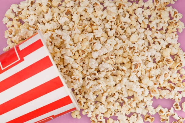 Popcorn nousee paperimaljasta vaaleanpunaiselle taustalle, näkymä ylhäältä. Kuppi popcornia on eristetty punaisella taustalla. Litteä pano. Kopioi tilaa. Elokuvakäsite
. - Valokuva, kuva