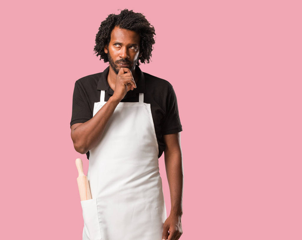 Handsome african american baker doubting and confused, thinking of an idea or worried about something - Photo, Image