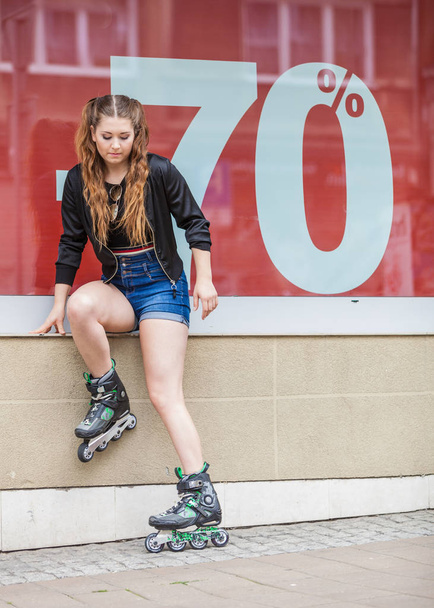 Teenage woman girl riding roller skates during summertime showing sale symbol on window. - Φωτογραφία, εικόνα