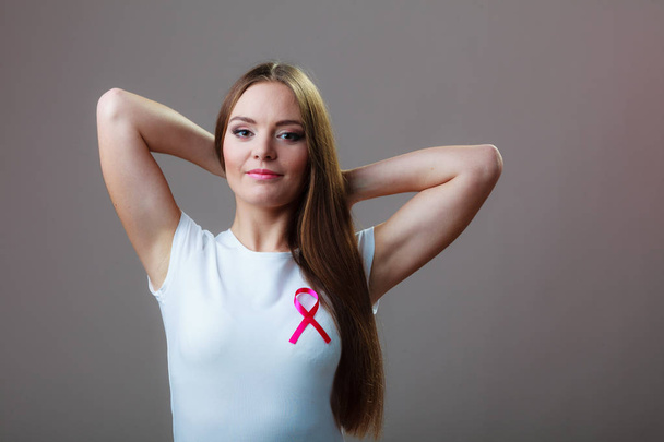 Woman wih pink cancer ribbon on chest. Healthcare, medicine and breast cancer awareness concept. Studio shot, grey background - Foto, Imagem