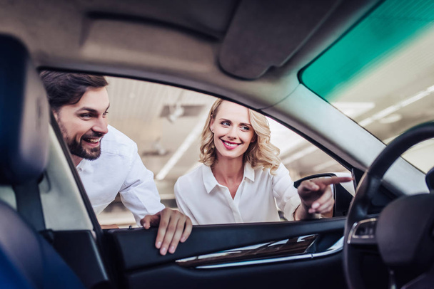 smiling couple looking at new car in dealership salon, view from car - Fotoğraf, Görsel