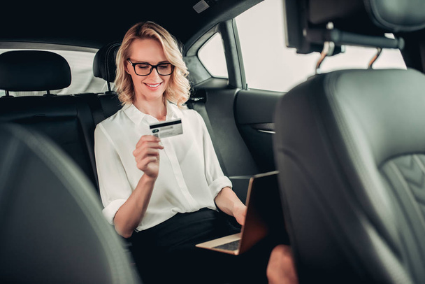 portrait of attractive businesswoman with laptop computer and credit card shopping online in the car - Фото, зображення