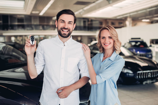 portrait of happy couple holding keys of new car in dealership salon - Foto, immagini