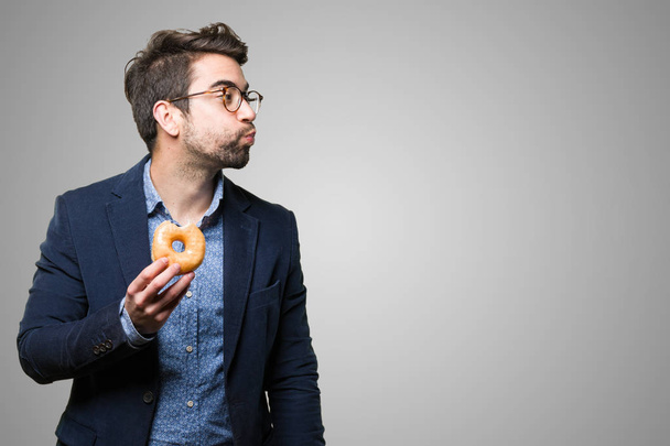 young man eating a doughnut on grey background - Photo, Image