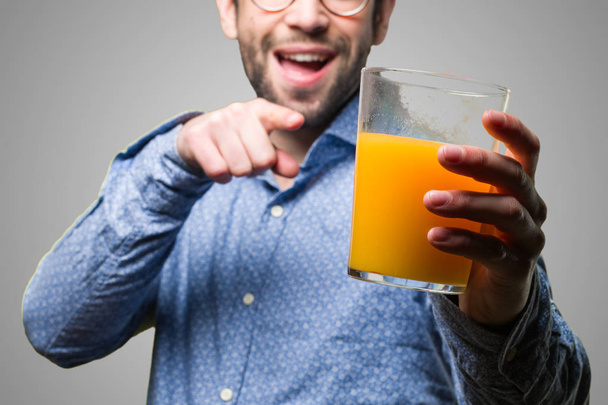 灰色の背景にジュースのガラスを指している若い男 - 写真・画像