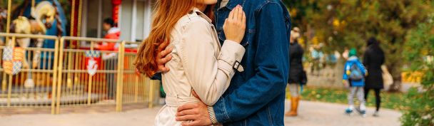 love, relationship, family and people concept - close up of couple the girl's hand is on the guy's shoulder, the man is hugging the woman. a pose of love and devotion. amusement park. a guy in jeans and a denim jacket, a girl in a light raincoat - 写真・画像