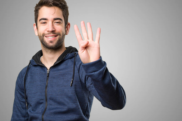 young man doing number four gesture on grey background - 写真・画像
