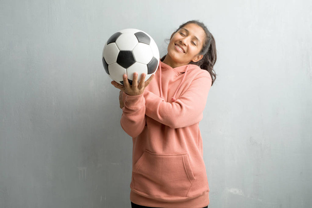 Молодая спортивная индианка у стены гордая и уверенная, указывающая пальцем, пример для подражания, понятие удовлетворения, высокомерия и здоровья. Проведение футбольный мяч, чтобы играть в игру
. - Фото, изображение