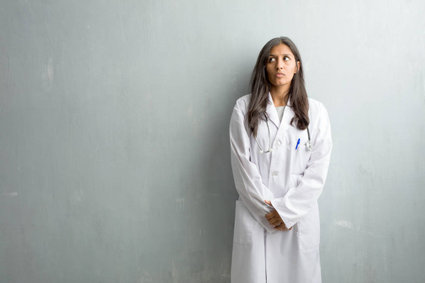 Młody lekarz indian kobieta przeciwko ścianie wątpiący i zdezorientowany, myślenia pomysłu lub martwi się o coś - Zdjęcie, obraz