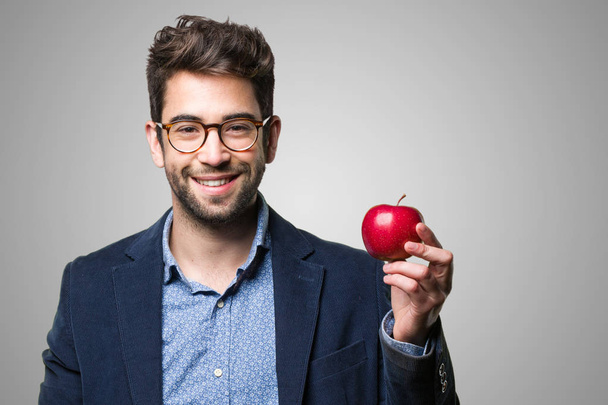 灰色の背景の赤いリンゴを保持している若い男 - 写真・画像